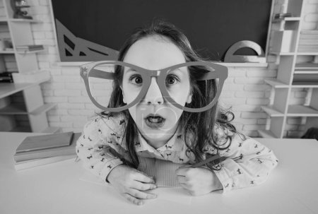 Photo for Funny geek surprised child school girl with fun glasses in classroom. Back to school - Royalty Free Image