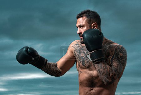 Photo for Sport boxing. Sportsman boxer fighting on sky background. Strong athletic man with boxing gloves punching. Boxer punch - Royalty Free Image