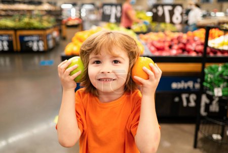 Foto de Comida saludable para familias jóvenes con niños. Retrato de un niño pequeño y divertido sosteniendo una bolsa llena de verduras frescas. Un chico está de compras en un supermercado. - Imagen libre de derechos