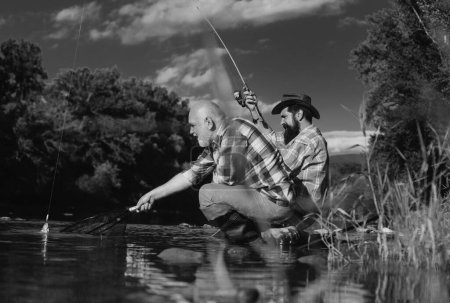 Photo for Two men friends fishing. Flyfishing angler makes cast, standing in river water. Old and young fisherman - Royalty Free Image