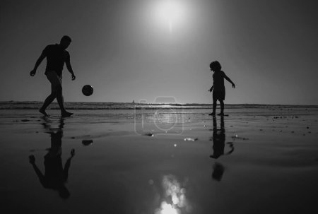 Photo for Father and son play soccer or football on the beach, silhouette on sunset. Dad and child having fun outdoors - Royalty Free Image