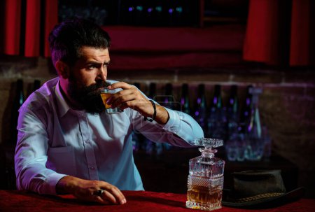 Foto de El hombre con barba y bigote tiene bebidas alcohólicas en el fondo de la barra. Concepto de servicio y alcoholismo - Imagen libre de derechos
