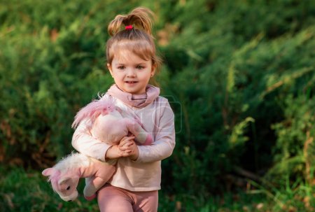Téléchargez les photos : Bébé fille mignonne avec jouet sur herbe verte en été. Petit enfant drôle sur la nature. Bonne enfance - en image libre de droit