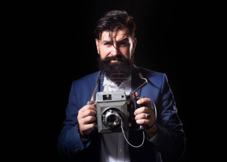 Téléchargez les photos : Photographe barbu avec un grand vieil appareil photo professionnel. Portrait d'homme photographe avec un vieil appareil photo vintage rétro isolé sur fond noir. Photographe rétro - en image libre de droit