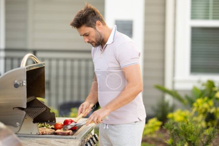 Grill chef cook. Guy with BBQ cooking tools. Barbecue and grill. Picnic and barbecue party. Chief cook with utensils for barbecue grill. Barbeque on holiday picnic. Man grilling a steak on BBQ