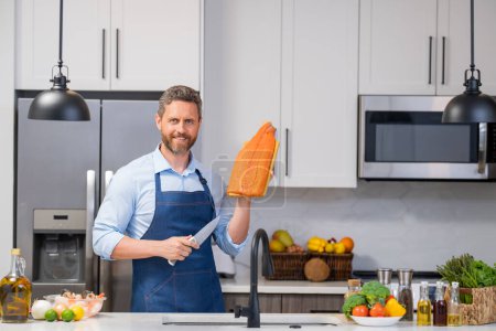 Photo for Cook in chef apron with raw fish salmon fillet on kitchen. Chef man in uniform cook apron on kitchen. Handsome man chef in uniform with chef hat cooking raw fish salmon fillet in the kitchen - Royalty Free Image