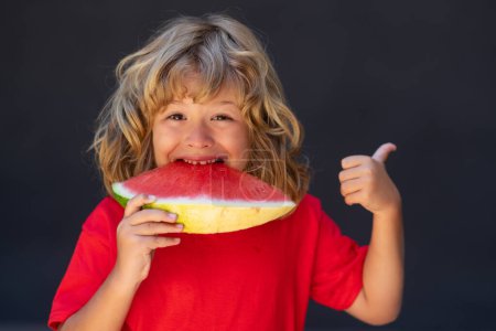 Foto de Un niño gracioso come sandía. El chico está recogiendo sandía sobre fondo gris - Imagen libre de derechos