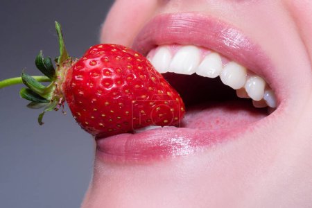 Foto de Frutas sexys de verano. Primer plano de sonrisa con dientes blancos y sanos. Fresa en los labios. Fresa roja en boca de mujer de cerca - Imagen libre de derechos