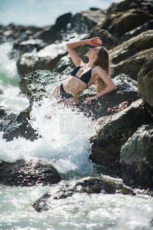 Téléchargez les photos : Femme sexy sur des rochers plage de pierre. Beau corps de femme en bikini sexy sur la plage. Sensuelle fille en bikini sur la mer. Photo de mode en plein air de belle coupe femme mince en mer - en image libre de droit