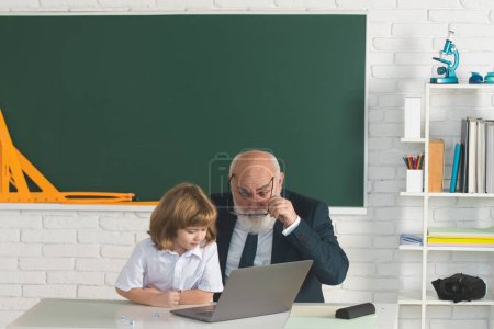 Photo for Teacher and pupil learning together in school. Boy from elementary school. Old and Young. Pupil study at school with old teacher - Royalty Free Image