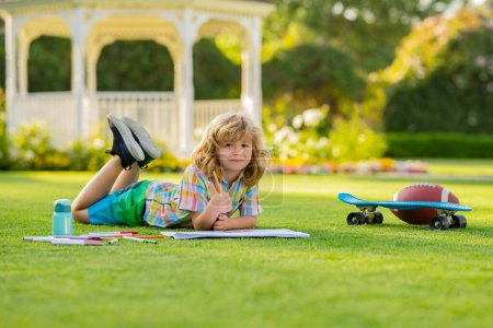 Photo for Child with artwork homework on playground. Child drawing picture with crayon in summer park outdoor. Happy little kid boy holding a brush to paint with toys for playing outdoor - Royalty Free Image