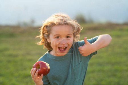 Téléchargez les photos : Pomme fraîche et mûre pour enfants. Enfant avec pomme extérieure. Garçon mangeant des pommes aux fruits. Il cueille des pommes. Enfants alimentation saine. Enfant mordant pomme fraîche dans le parc d'été - en image libre de droit