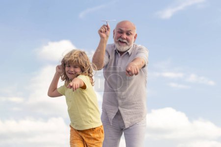 Photo for Old grandfather and young child grandson playing with toy paper plane against summer sky background - Royalty Free Image