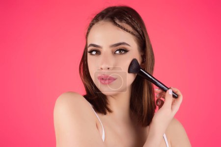 Téléchargez les photos : Beautiful woman applying make-up powder on the cheek. Cosmetic powder brush. Perfect skin and natural makeup - en image libre de droit