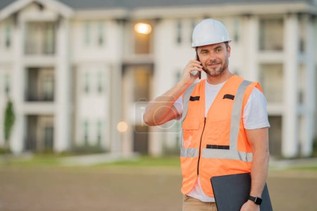 Photo for Builder using phone. Builder at construction site. Buider with helmet on construction outdoor. Worker at construction site. Bilder in hardhat - Royalty Free Image