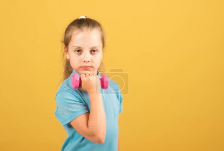 Foto de Niña niña está haciendo ejercicios con mancuernas sobre fondo de estudio amarillo - Imagen libre de derechos