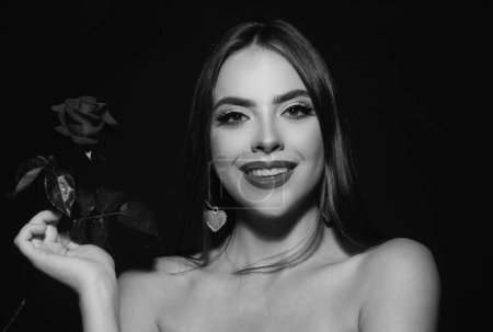Foto de Mujer sonriente con los labios rojos hombro desnudo y flor de rosa. Retrato de belleza de moda sobre fondo negro de estudio - Imagen libre de derechos