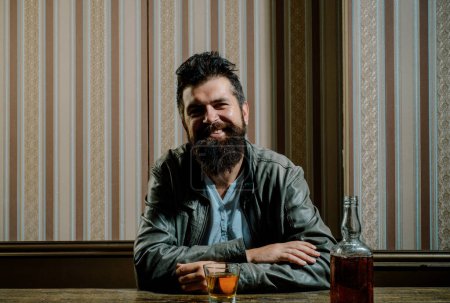 Téléchargez les photos : Un barbu joyeux boit du whisky cher. élégant élégant barbu homme tient verre de whisky dans le pub - en image libre de droit