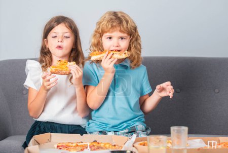 Téléchargez les photos : Les enfants mangent des pizzas. Un garçon et une fille mangent de la pizza. Déjeuner enfants - en image libre de droit
