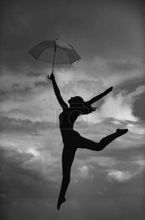 Photo for Silhouette of woman with umbrella doing stretching up exercise outdoors. Dance studio - Royalty Free Image