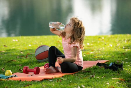 Téléchargez les photos : Enfant sportif. Enfant manger des aliments sains, boire de l'eau après l'exercice - en image libre de droit