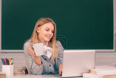 Photo for Female student drinking coffee or tea on lesson lecture in classroom at high school or college - Royalty Free Image