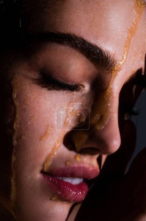 Photo for Sensual young woman face with honey drop close up. Sexy model with honey drip on face - Royalty Free Image
