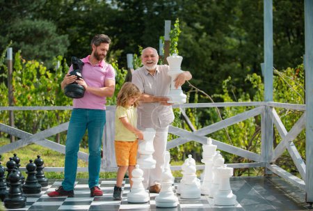 Foto de Abuelo padre e hijo jugando ajedrez. Hombres en diferentes edades jugando ajedrez juego de mesa. Familia de fin de semana. Generación de los hombres concepto - Imagen libre de derechos