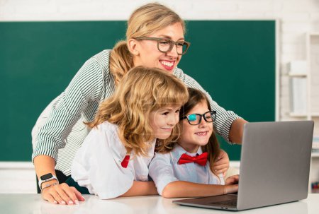 Photo for First day at school. Cute little boy from elementary school and tutor teacher studying lesson on laptop in class. Back to school - Royalty Free Image