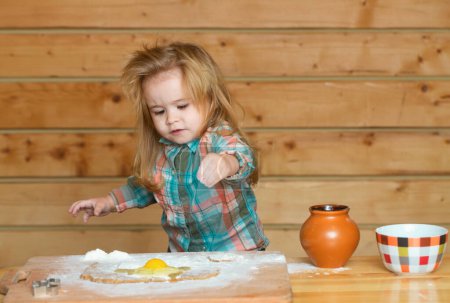 Foto de Lindo bebé jugando con harina en la cocina de madera. Cocina infantil - Imagen libre de derechos