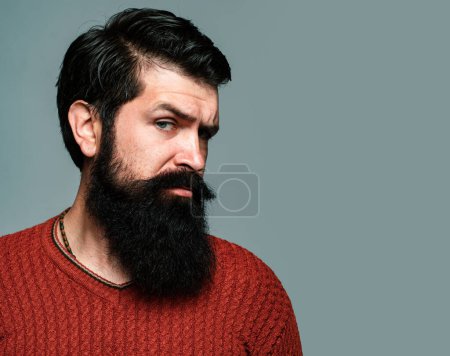 Foto de El retrato del hombre seguro serio tiene la barba y el bigote, se ve serio, aislado en gris. Hipster chico modelos en estudio - Imagen libre de derechos