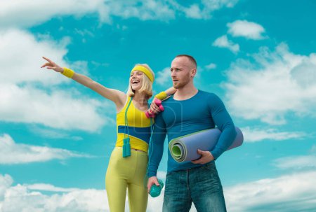 Téléchargez les photos : Portrait de jeune couple sportif heureux tenant haltères et tapis de fitness en plein air - en image libre de droit