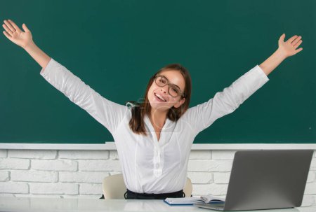 Téléchargez les photos : Portrait d'une jeune étudiante émerveillée, les mains levées dans la salle de classe - en image libre de droit