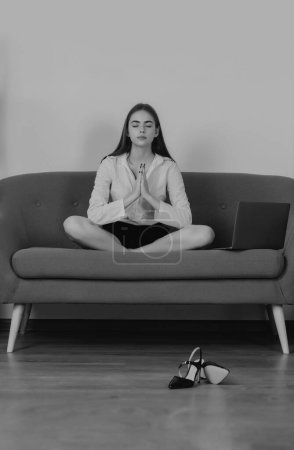 Foto de Mujer de la meditación en un lugar de trabajo moderno haciendo ejercicio de yoga en el sofá en el lugar de trabajo en una oficina moderna. Empleado siente equilibrio armonía relajación. Calma contable chica en el sofá en la oficina - Imagen libre de derechos