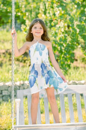 Photo for Little girl swinging on a summer sunny day. Child dreaming on swing. Child swinging on playground on sunny summer day in a park. Summer outdoor activity. Kid playing - Royalty Free Image