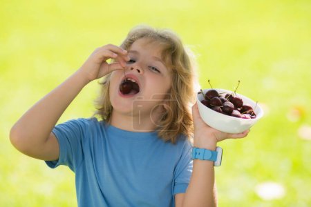 Photo for Cherry and cute child. Cherry for kids. Child hold plate cherries on summer green grass background - Royalty Free Image