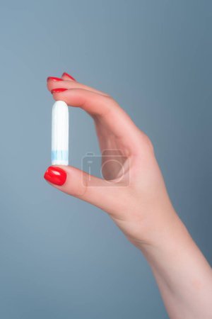 Photo for Hand holding menstruation tampon. Womens menstrual cramps. Feminine tampon. Hygienic tampon in female hand close-up. Critical days, menstrual period. Gynecological health care. Cotton tampon - Royalty Free Image