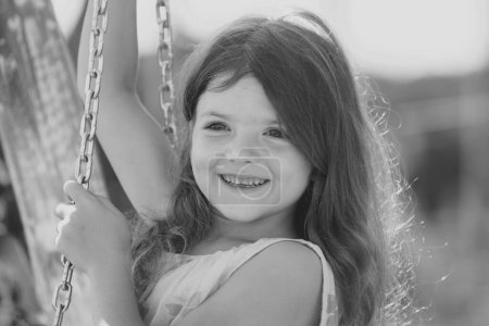 Téléchargez les photos : Happy child girl laughing and swinging on a swing at summer garden. Happy kid having fun outdoors. Close up portrait of a beautiful child girl dreaming. Childhood, summer leisure - en image libre de droit