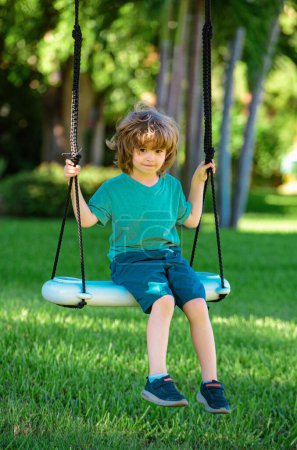 Foto de Niño jugando al aire libre. Los niños se balancean en el patio. Feliz lindo niño balanceo y divertirse saludable actividad de vacaciones de verano - Imagen libre de derechos
