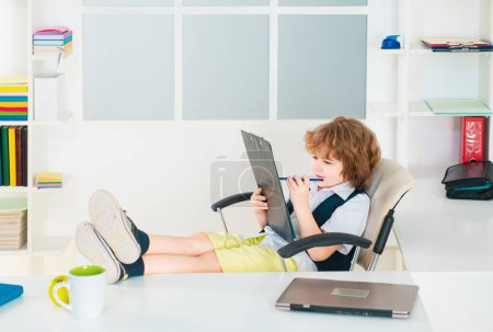 Téléchargez les photos : Petit garçon d'affaires prospère assis au bureau. Enfant en costume comme un pigiste - en image libre de droit