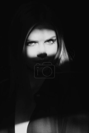 Photo for Young woman posing at studio over black background. Light and shadow. Fashion portrait of beautiful woman with dark light on face. Creative portraits with shadow and light over womans face, eyes on - Royalty Free Image