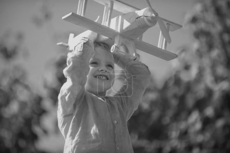 Foto de Niño piloto con juguete avión sueña con viajar en verano en la naturaleza. Los niños sueñan. El niño juega con un avión de juguete y sueña con convertirse en piloto. Niño rubio, cara de emoción sonriente - Imagen libre de derechos