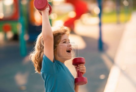 Photo for Kids sport training on playground outdoor. Sport activities at leisure with children. Sporty kid boy holding dumbbells - Royalty Free Image
