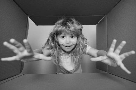 Foto de Niño divertido está abriendo regalo y mirando dentro de la caja de cartón. Niño con caja abierta tomar a mano regalo - Imagen libre de derechos