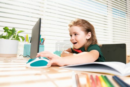 Foto de Asombroso niño de la escuela usando el ordenador portátil preparando tarea. Alumno feliz haciendo la escuela en casa, buscar información en línea en el ordenador - Imagen libre de derechos