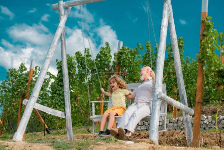Téléchargez les photos : Grand-père et fils se balancent dans le jardin. Grand-père et petit-enfant jouant sur swing - en image libre de droit