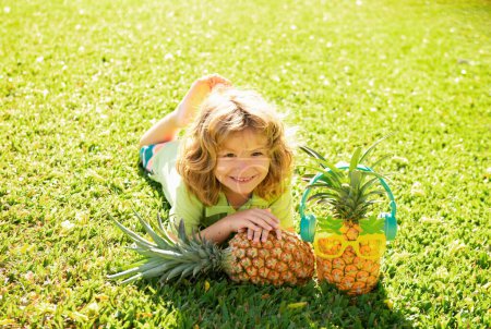 Téléchargez les photos : Enfant garçon tenant un ananas posant fond nature d'été avec de l'espace de copie. Fruits sains pour enfants concept - en image libre de droit