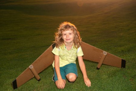 Téléchargez les photos : Voyageur enfant avec des ailes de sac à dos. Enfant jouant pilote aviateur et rêve à l'extérieur dans l'herbe - en image libre de droit