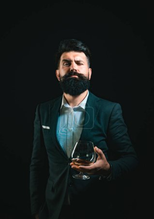 Photo for Cheerful bearded man is drinking expensive cognac. Confident well-dressed man with glass of cognac - Royalty Free Image