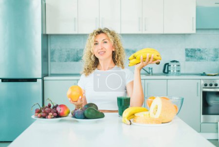 Foto de Concepto de alimentación saludable. Joven sonriente sostiene plátano y frutas de naranja en la cocina. Comer y comida saludable. Mañana comer frutas para bajar de peso - Imagen libre de derechos